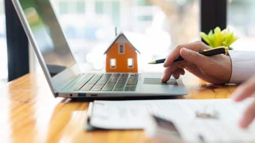 person sitting at a computer with documents and a model of a house in background - mistakes personal representatives make concept